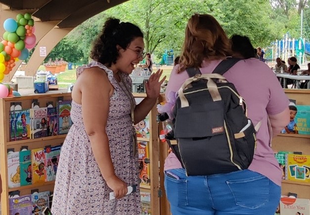 Library staff greets patrons with smile by a colorful book display outside