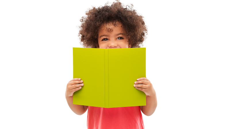 Young curly hair child hides his smile behind an open book