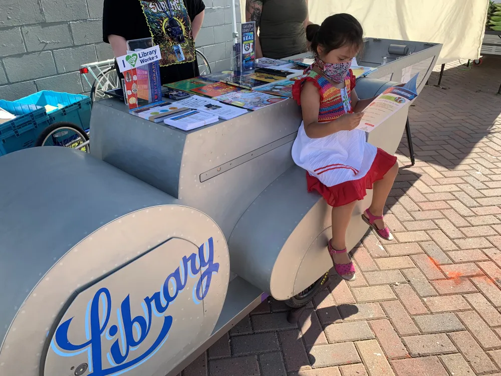 A girl reading by library bike at the market