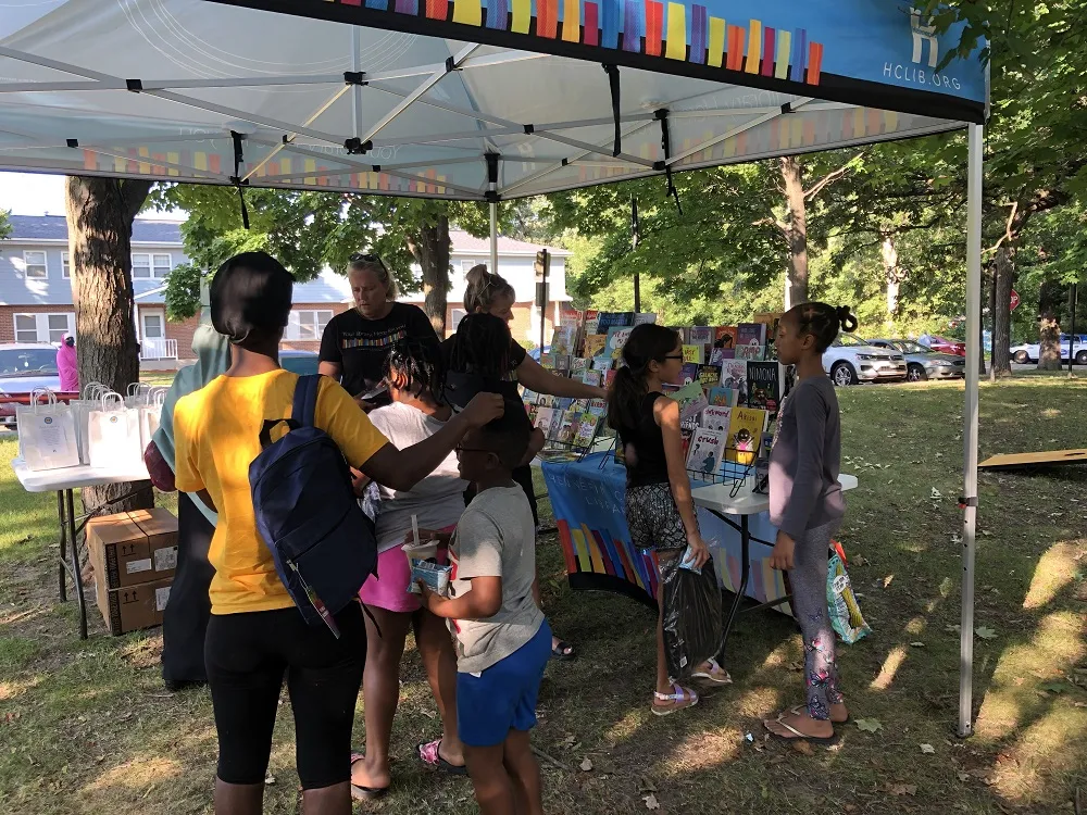 Children and a parent gather under the library tent to get free books at Luxton Park