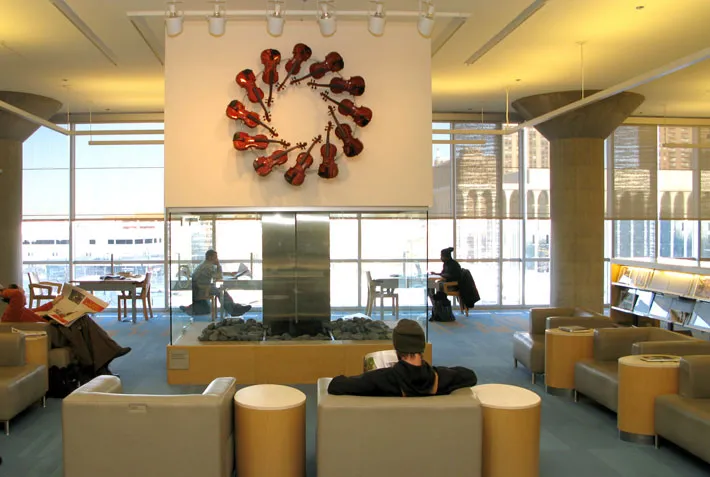 Library patrons read, lounge and work at Minneapolis Central Library below an art installment of string instruments on the wall.