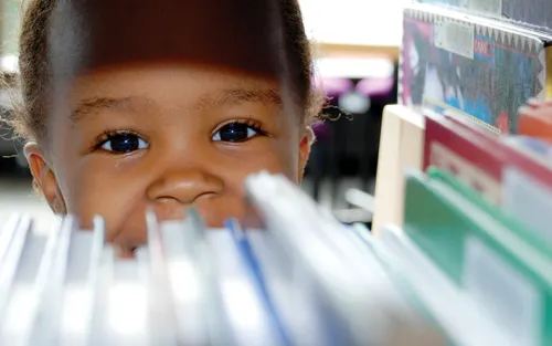 Young girl peeking through a bookshelf