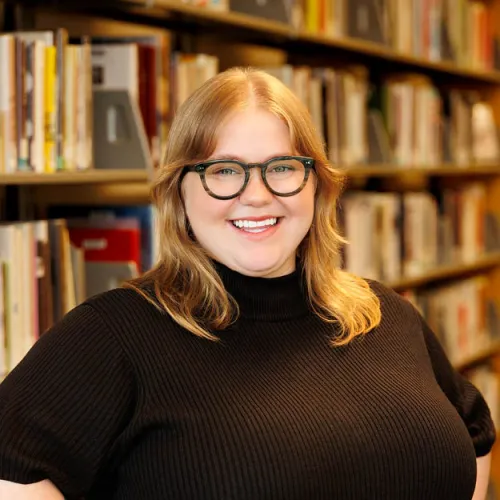 Kelsey Connelly smiling in front of the stacks at Minneapolis Central Library