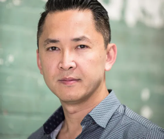 Headshot of author Viet Thanh Nguyen in a blue shirt in front of a green wall