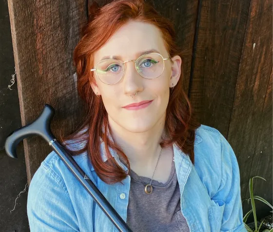 Headshot of author torrin greathouse in a blue button down shirt with a cane