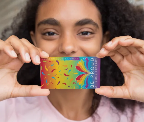 Happy library patron holding 'Be Proud' library card