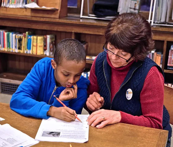 An adult helping a child with homework by the table surrounded by books