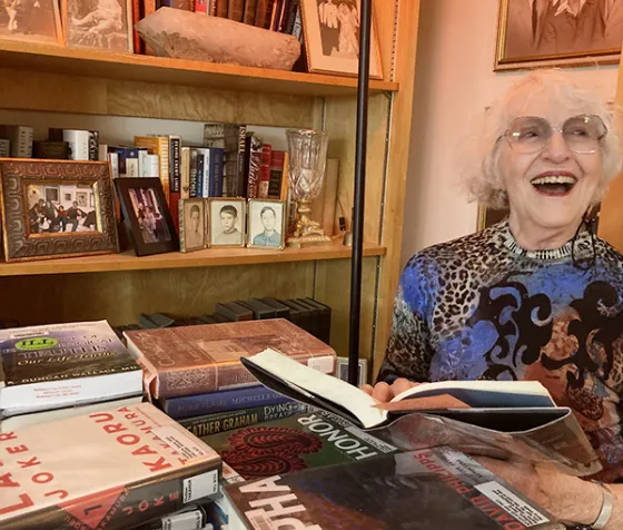 Nancy with her latest library books. Behind her is a photograph of her three smiling sons.