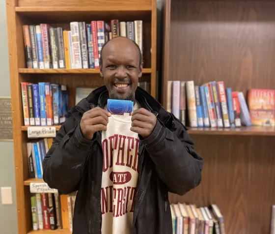 A man smiles holding his new library card at the Opportunity Center shelter. 