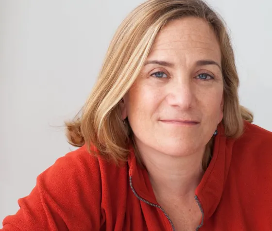 In this headshot, Tracy Chevalier wears a red top and smiles into the camera in front of a plain backdrop.
