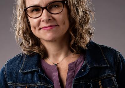 Headshot of author Kim Heikkila in a blue coat in front of a gray background