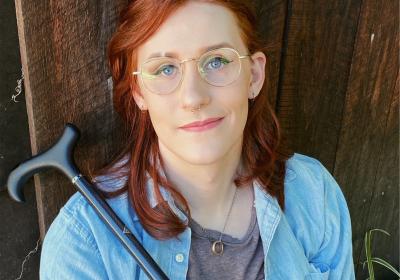 Headshot of author torrin greathouse in a blue button down shirt with a cane