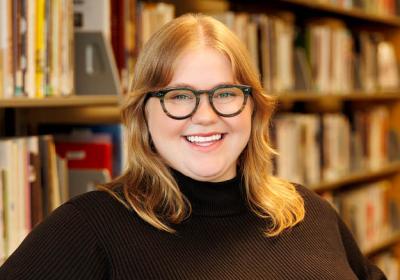 Kelsey Connelly smiling in front of the stacks at Minneapolis Central Library