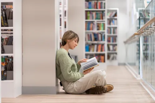Reader sits among the stacks, reading.