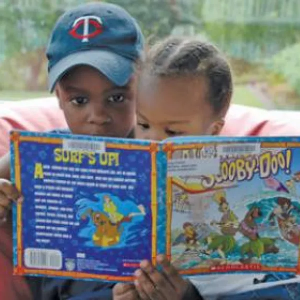 Two small children sitting on a been bag chair reading a kids book together