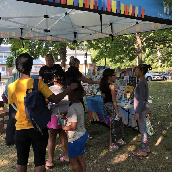 Children and a parent gather under the library tent to get free books at Luxton Park