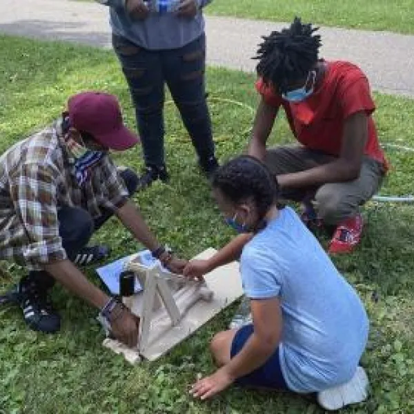 A group of kids siting on the grass and working on a STEM project during summer learning in the park