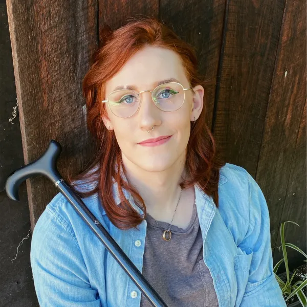 Headshot of author torrin greathouse in a blue button down shirt holding a cane